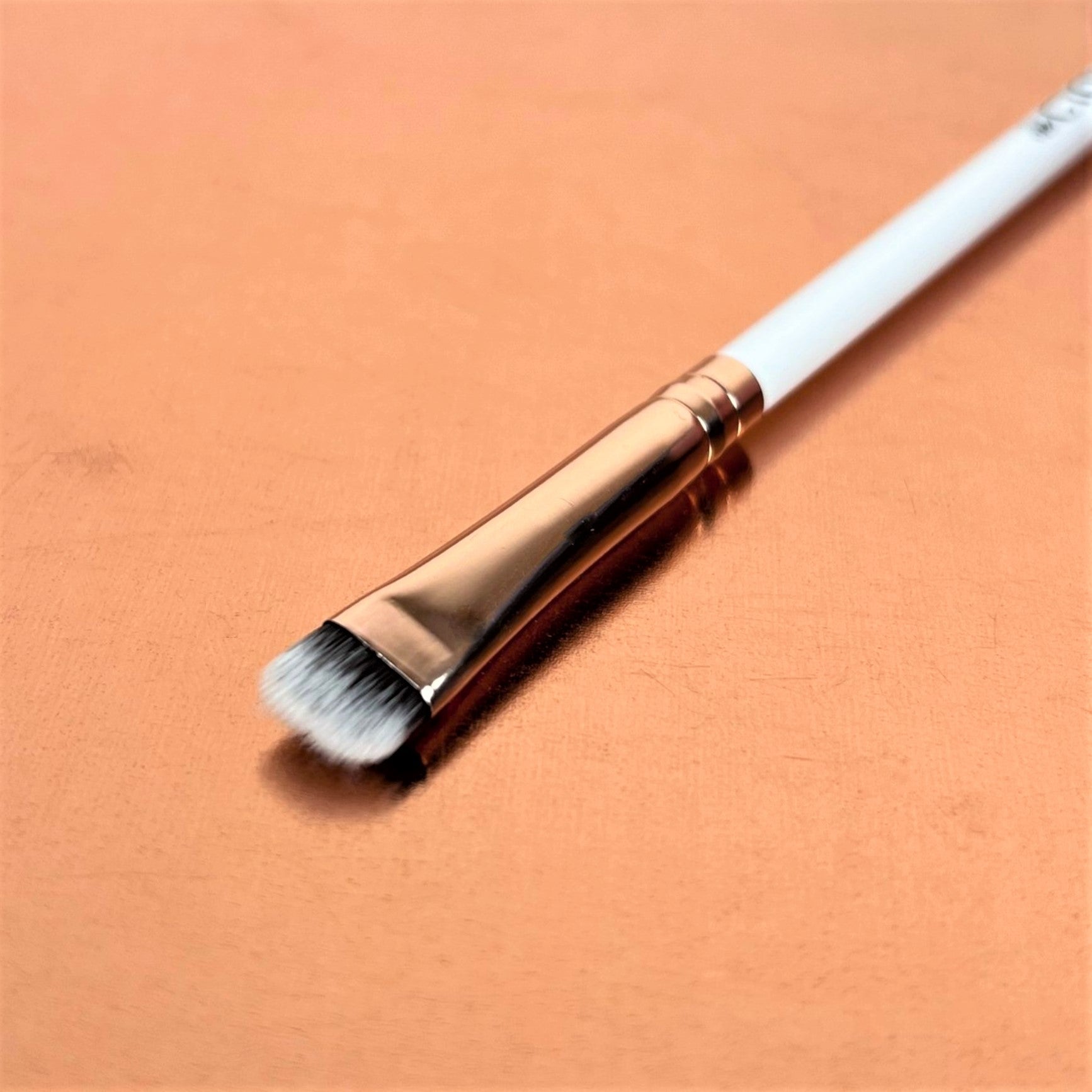 A single chisel smudger makeup brush with a white handle and synthetic bristles, displayed on an orange background.